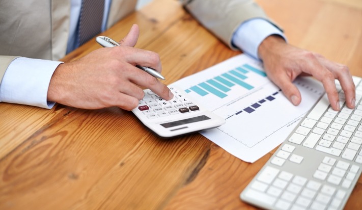 Man with a calculator, data sheets, and computer keyboard, suggesting business valuation